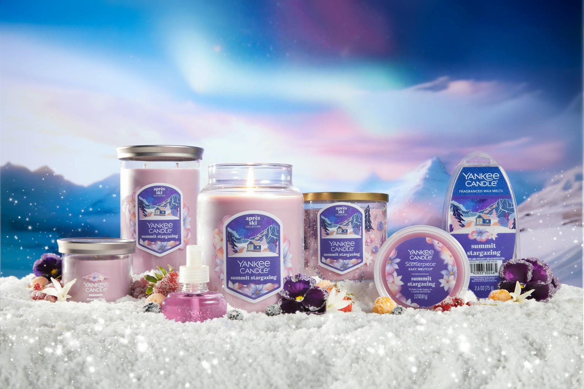 an array of summit stargazing products and candles on a snowy surface with flowers and berries and with mountains in distance