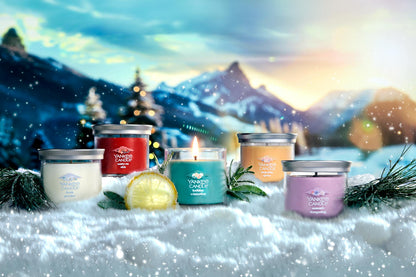 Apres Ski Collection Fresh Powder Signature Small Tumbler Candle, Santa on Skis Signature Small Tumbler Candle, Holiday Winterfest Signature Small Tumbler Candle, Slopeside Spritz Signature Small Tumbler Candle, and Summit Stargazing Signature Small Tumbler Candle in snow surrounded by mountains, slices of lemon, and branches