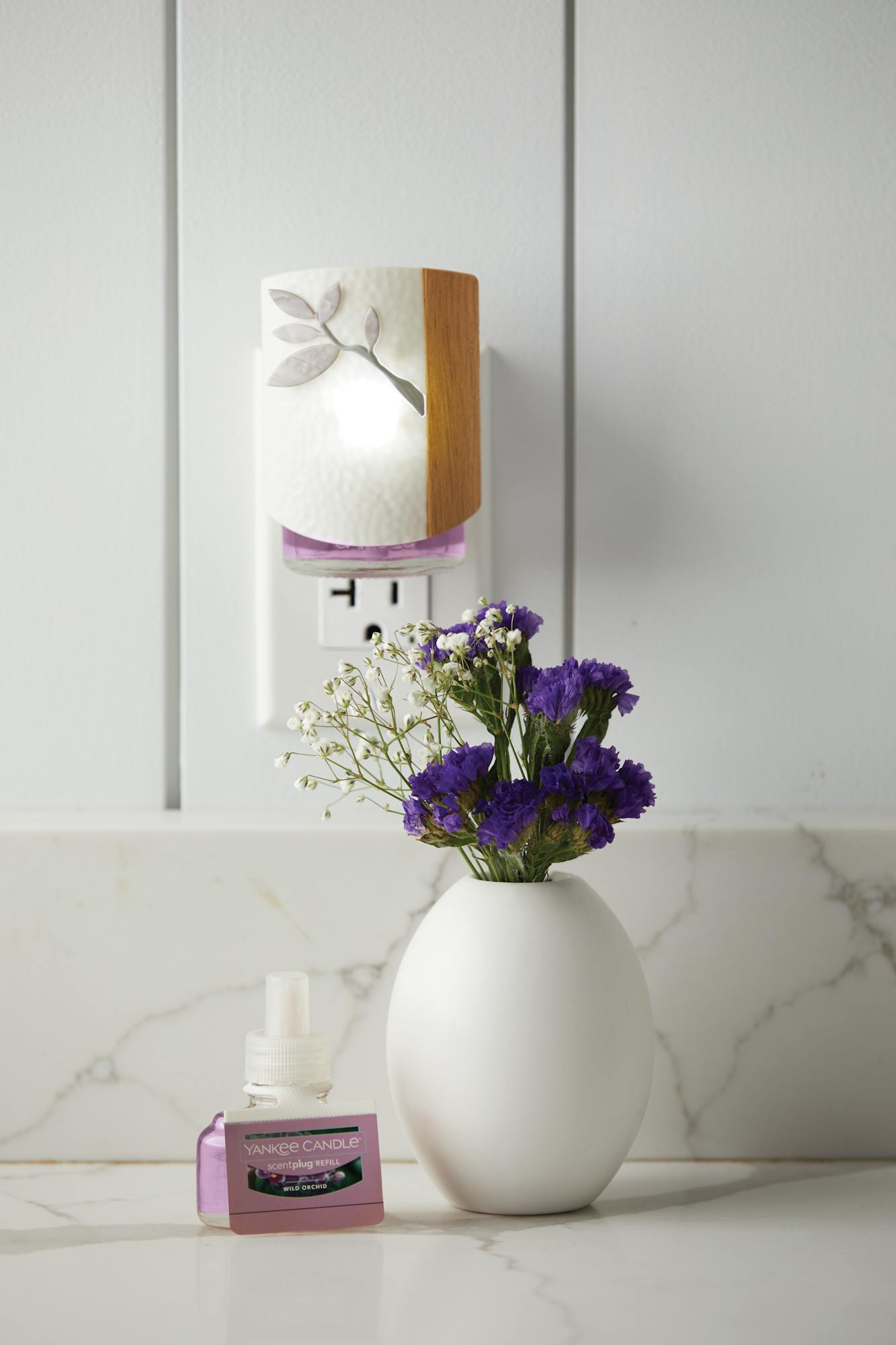 two wild orchid scentplug refills and a dogwood scentplug diffuser next to a vase of purple and white flowers