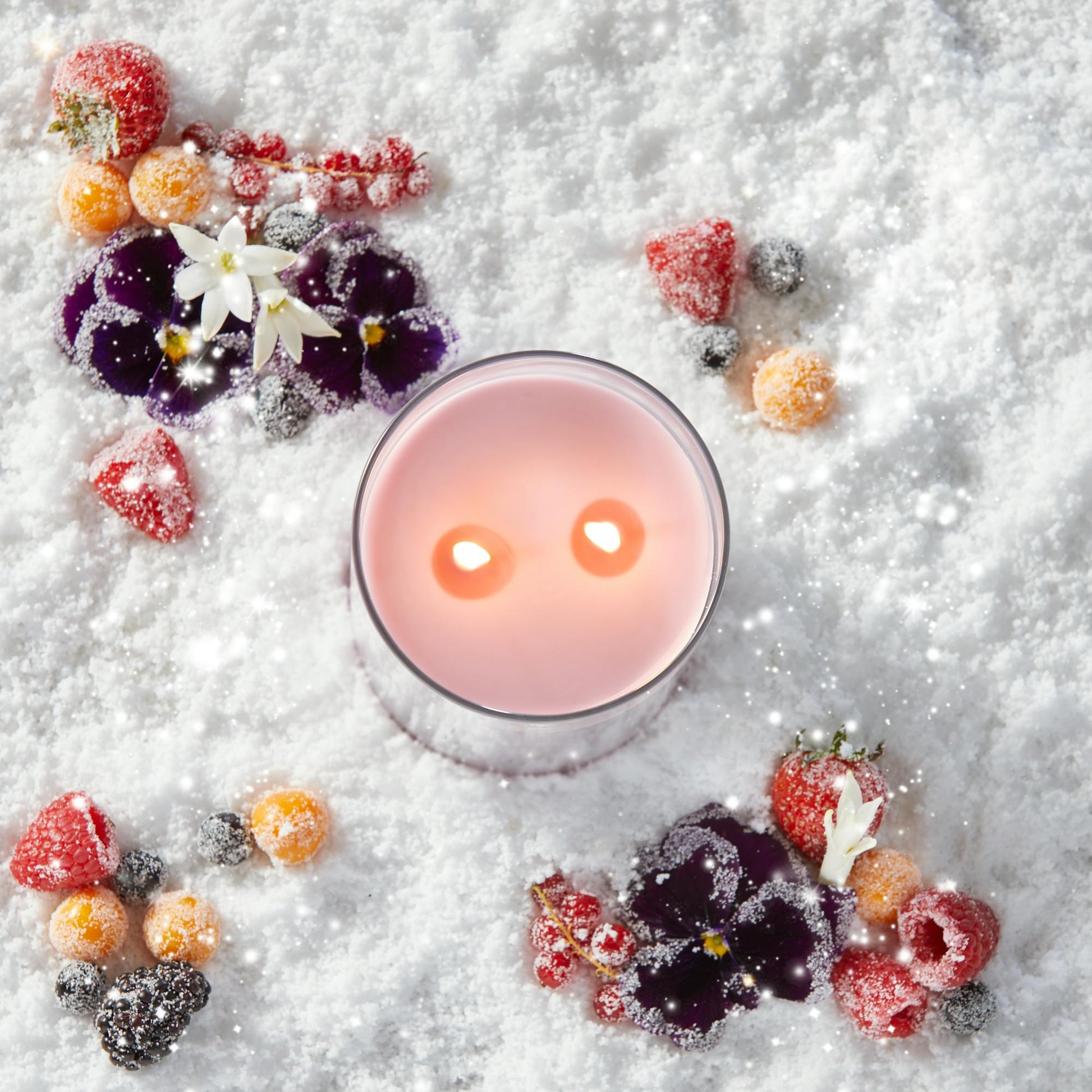 a pink-colored Signature Large Tumbler Candle in snow surrounded by berries