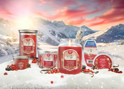 an array of santa on skis products on a snowy surface with vanilla beans and cardamom and red berries with mountains in distance