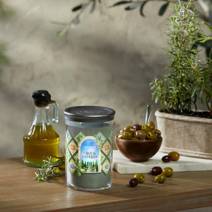 Hello, Italy! Collection Olive & Cypress Signature Large Tumbler Candle on a table with a jar of olive oil and a bowl of olives