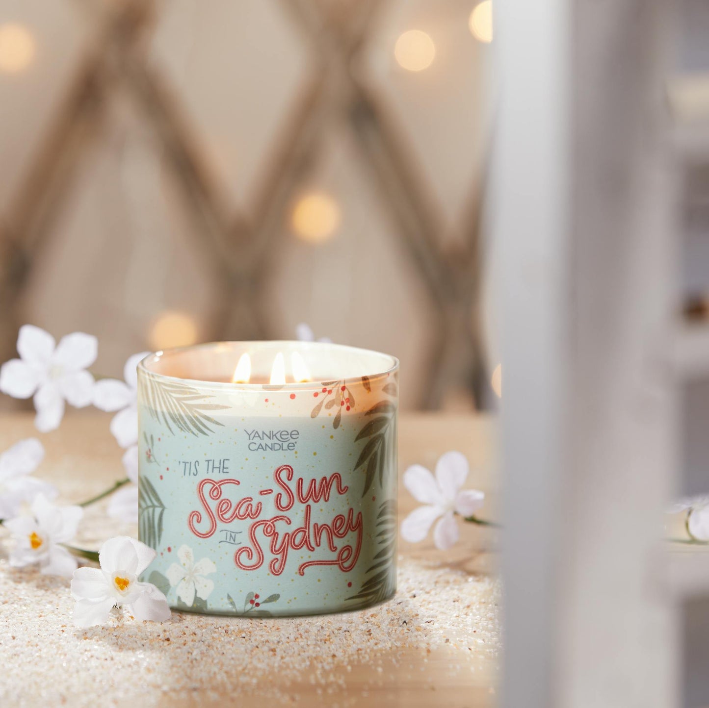 tis the sea-sun in sydney three wick candle on table with white flowers and sand