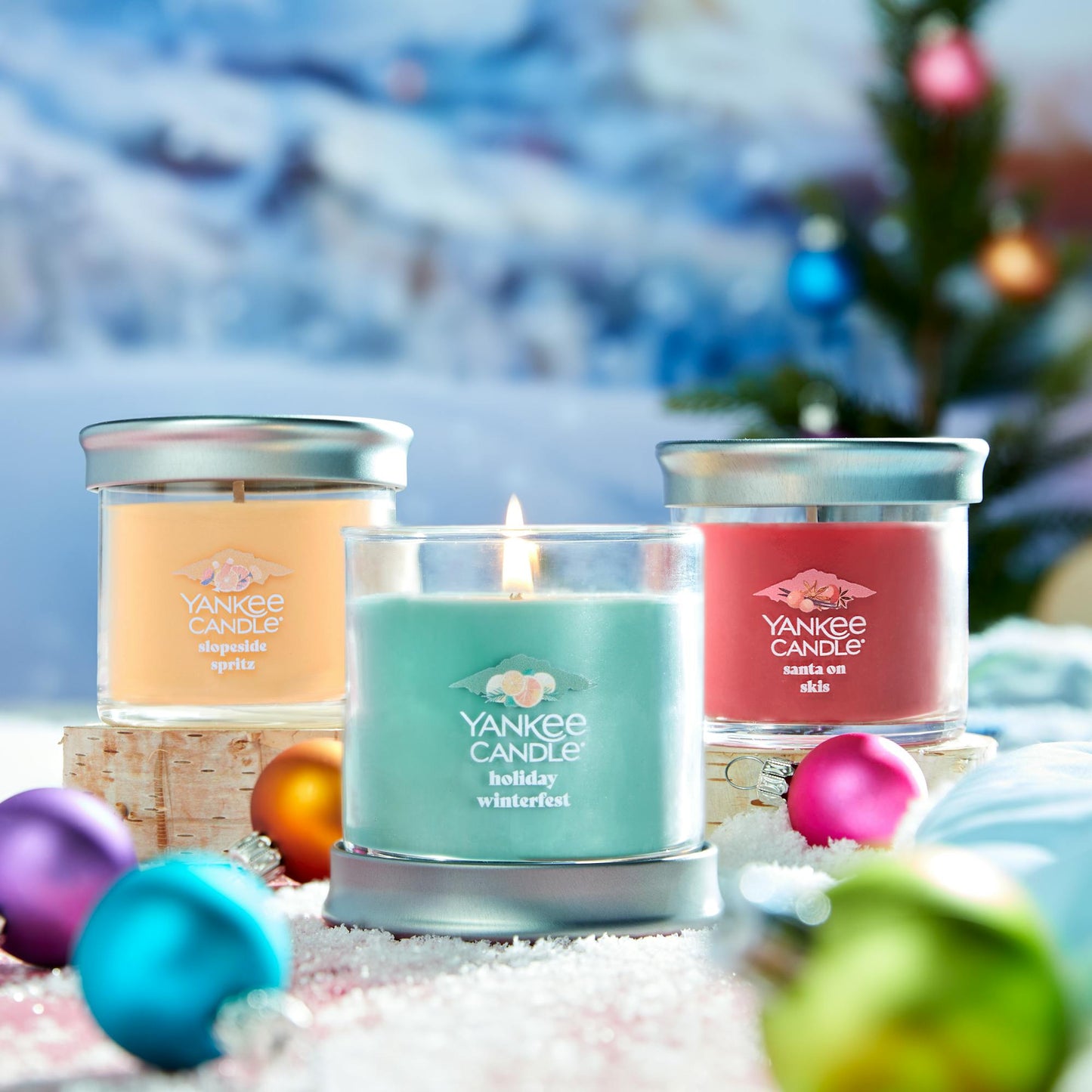 three apres ski small tumbler candles with ball ornaments in a snowy scene