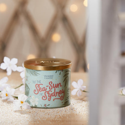 tis the sea-sun in sydney three wick candle on table with white flowers and sand